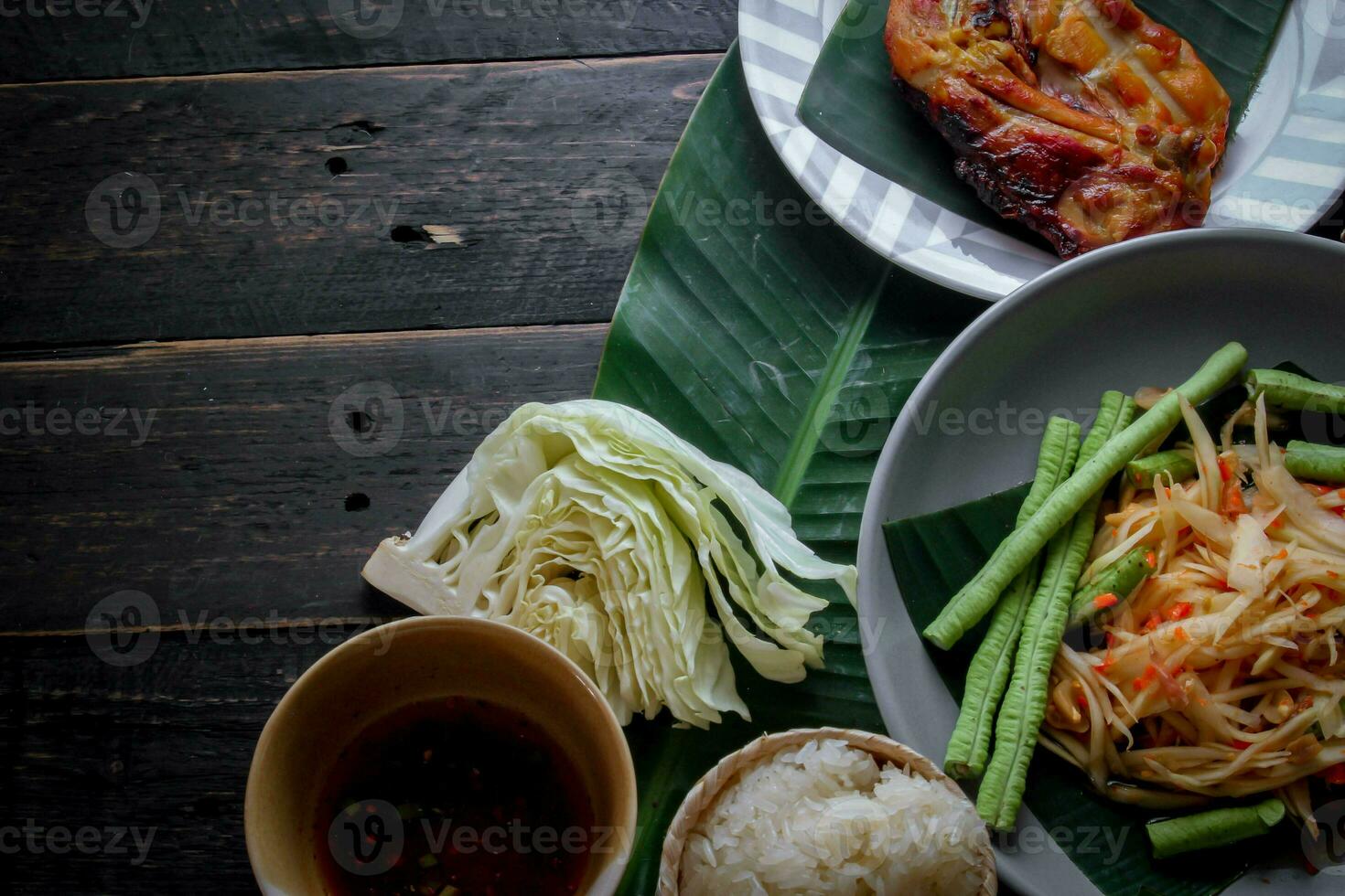 Thai food dish both in Thailand and Asia Papaya Salad or as we call it Somtum is complemented with grilled chicken and sticky rice with fresh stir-fries. Served on the black wooden table. photo