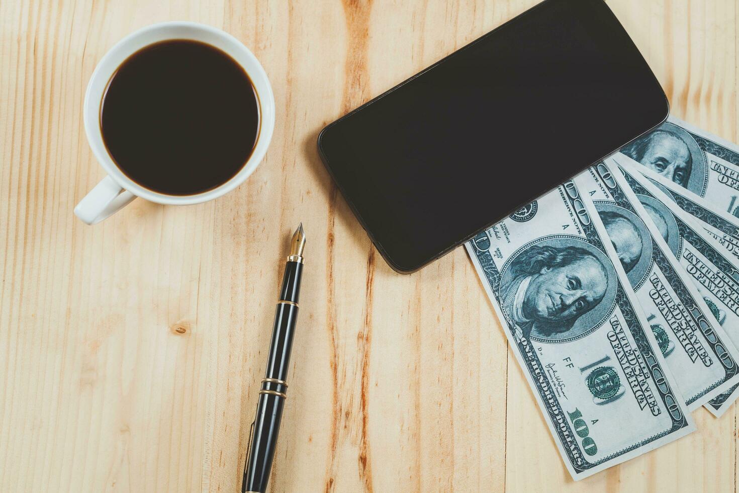 mobile on bank note with fountain pen and hot coffee on wood table.business concept. photo