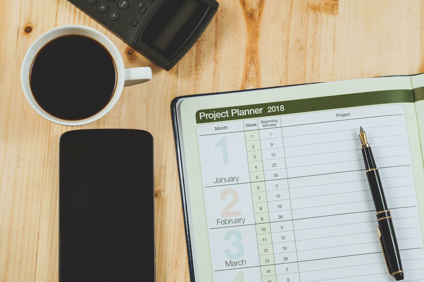 personal project planner with fountain pen and hot coffee on wood table. photo