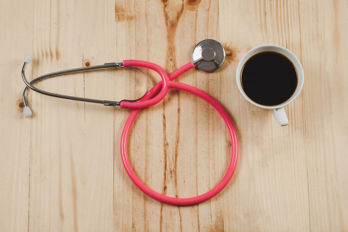 rosado estetoscopio es médico instrumentos con caliente café en de madera. foto