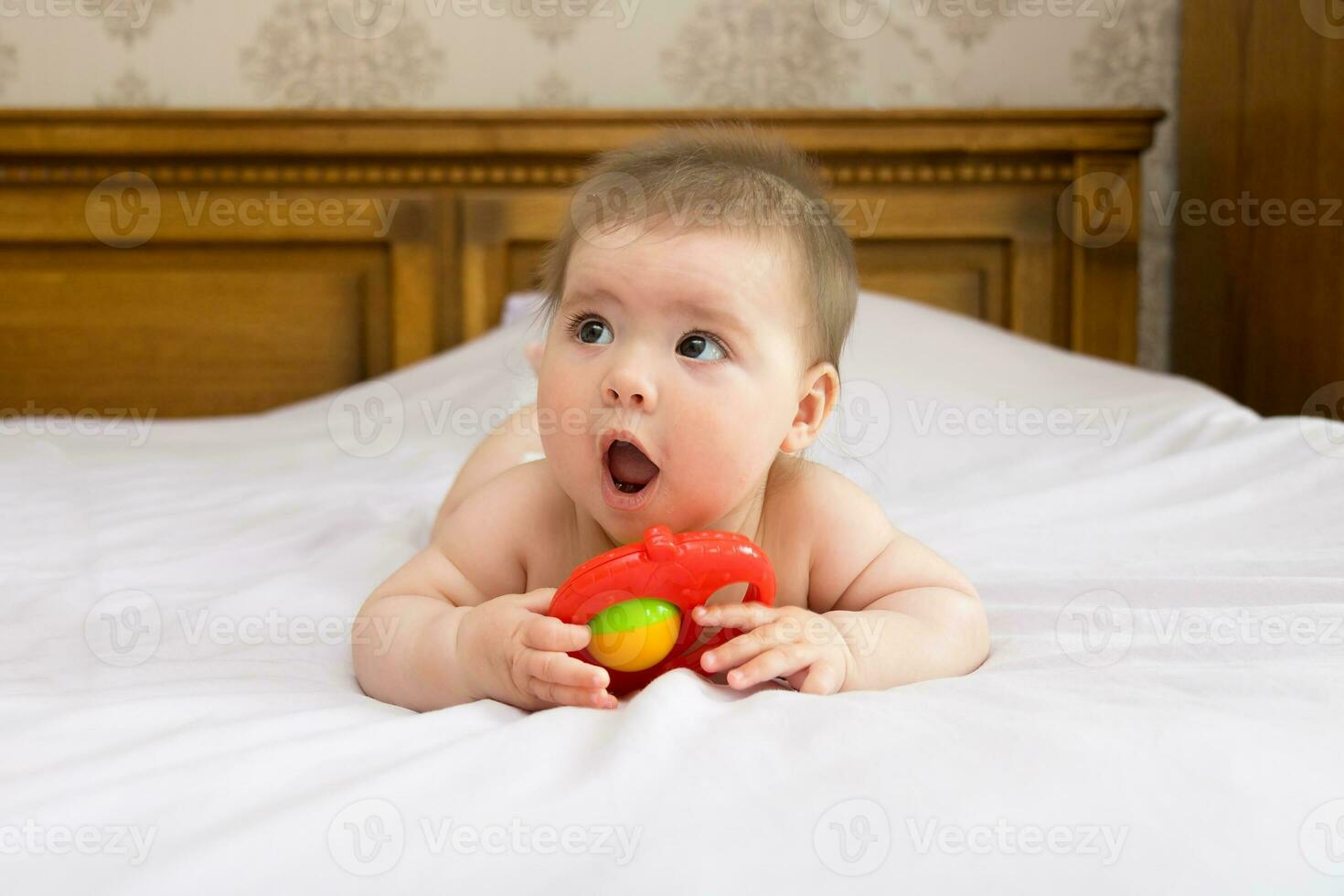 baby girl on the bed in the bedroom has fun playing with a rattle photo