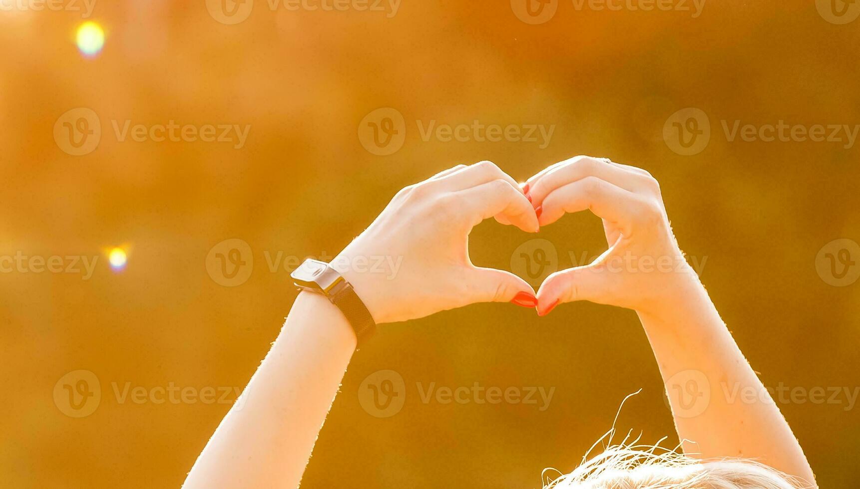 shot of heart symbol created from woman's hands over bright yellow foliage background at fine sunny autumn day. Have a good mood and be ready to fall in love at every season photo