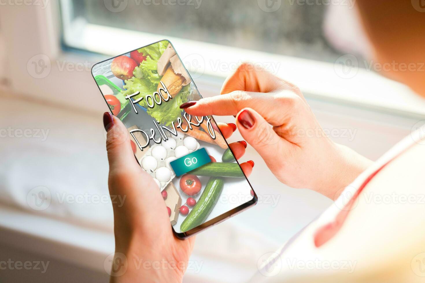 Girl ordering pizza online on smartphone, with table and coffee and plant in background photo