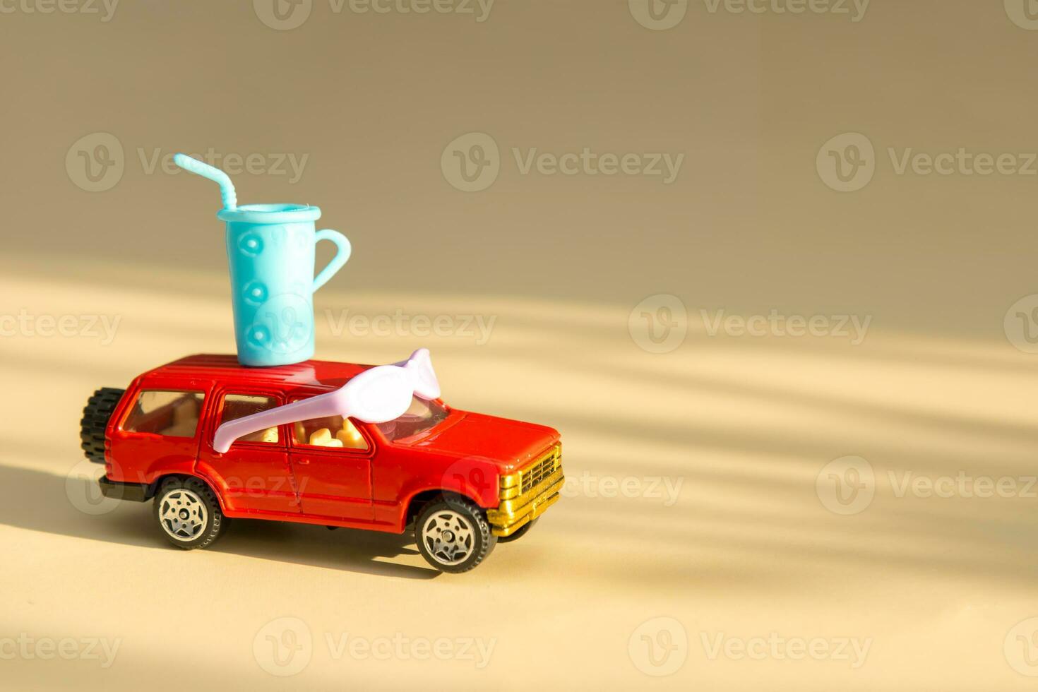 toy car in sunbeams in sunglasses and a glass of cocktail on the roof on a light beige background with copy space, holiday content photo
