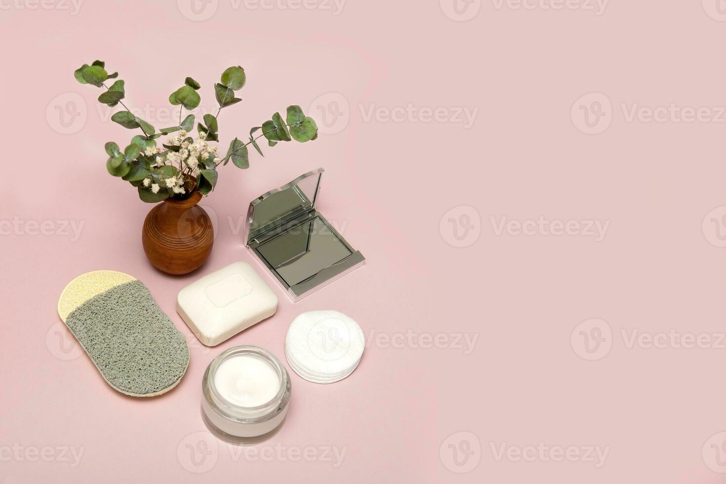 cosmetic accessories face sponge, soap, face cream, mirror, cotton pads on a soft pink background with a vase of greenery and copy space photo