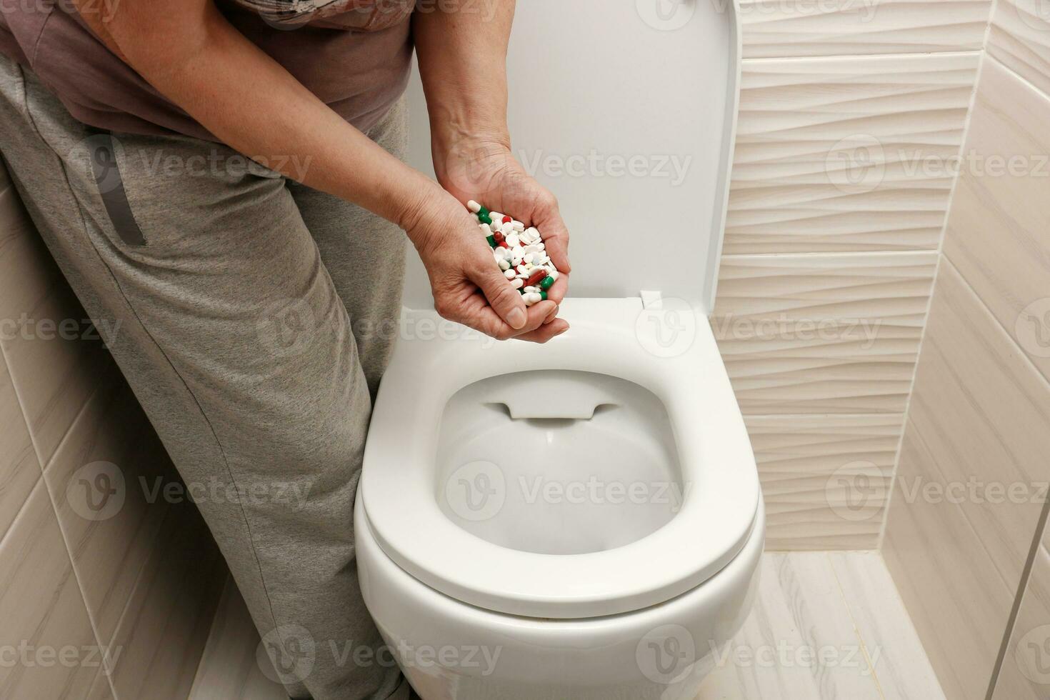 female hands throw a handful of pills into the toilet photo