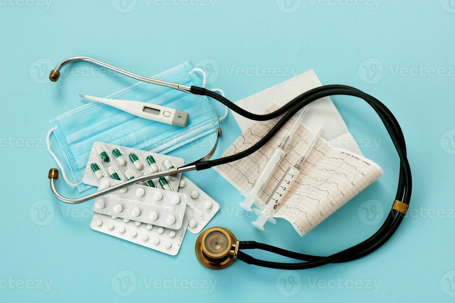 pills, phonendoscope, thermometer, mask, cardiogram, syringes on a blue background, modern medicine photo