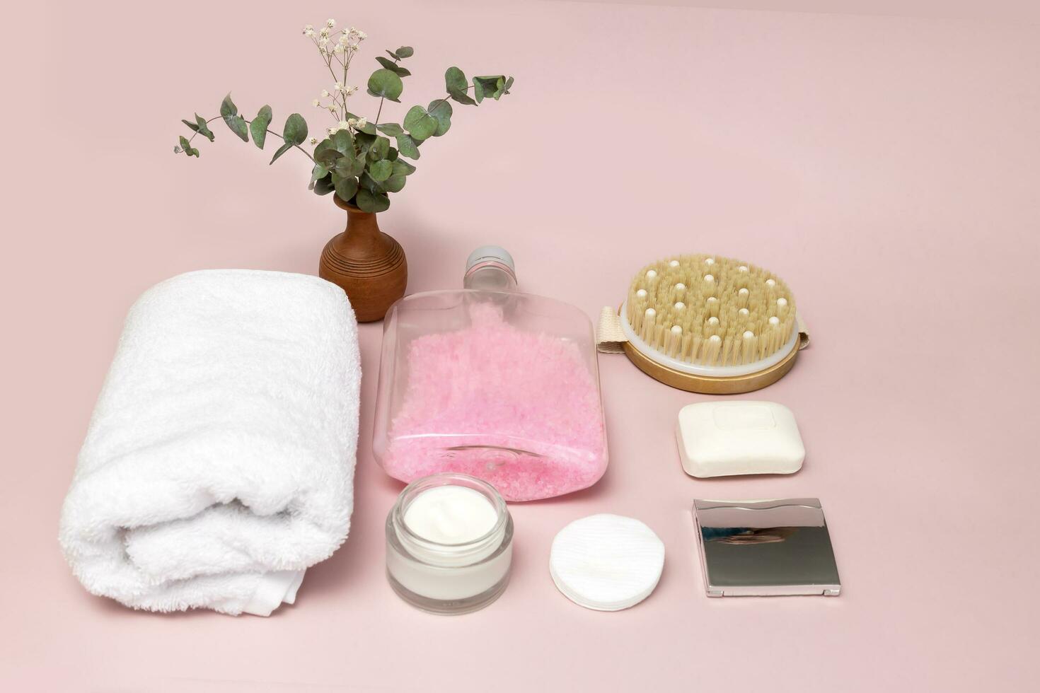 towel, cream, cotton pads, massager, vase of flowers, bath accessories on a pale pink background photo