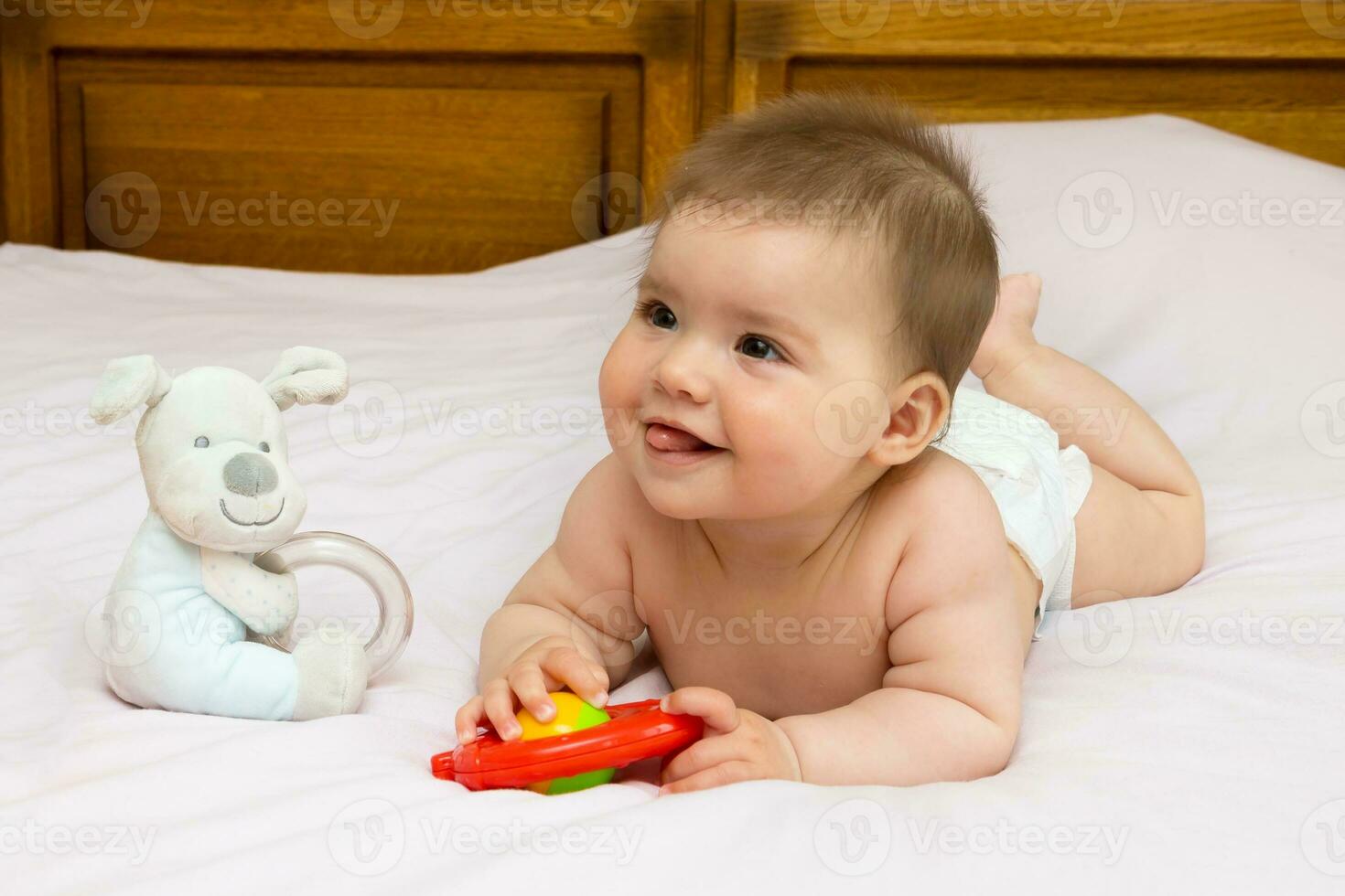 baby girl on mother's bed playing with a rattle photo