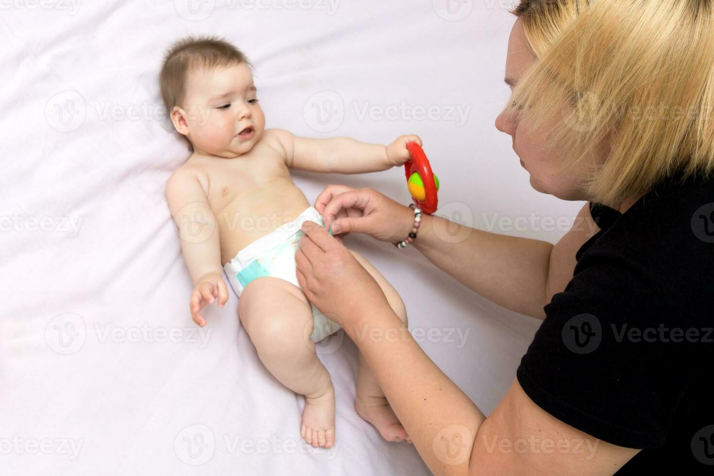 mom puts a diaper on the baby girl on the bed photo