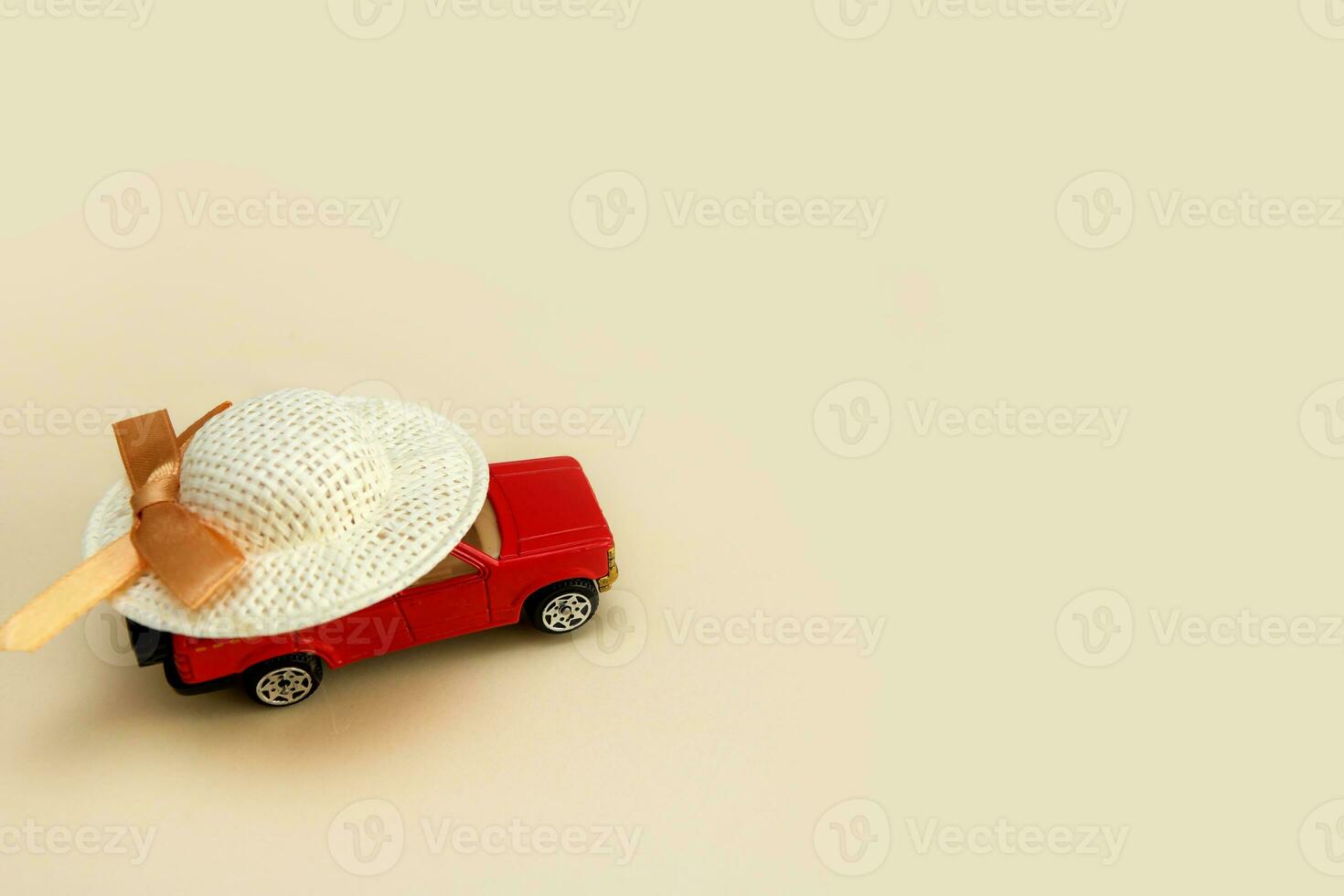 red toy car in a straw hat on a light beige background with copy space, car travel photo