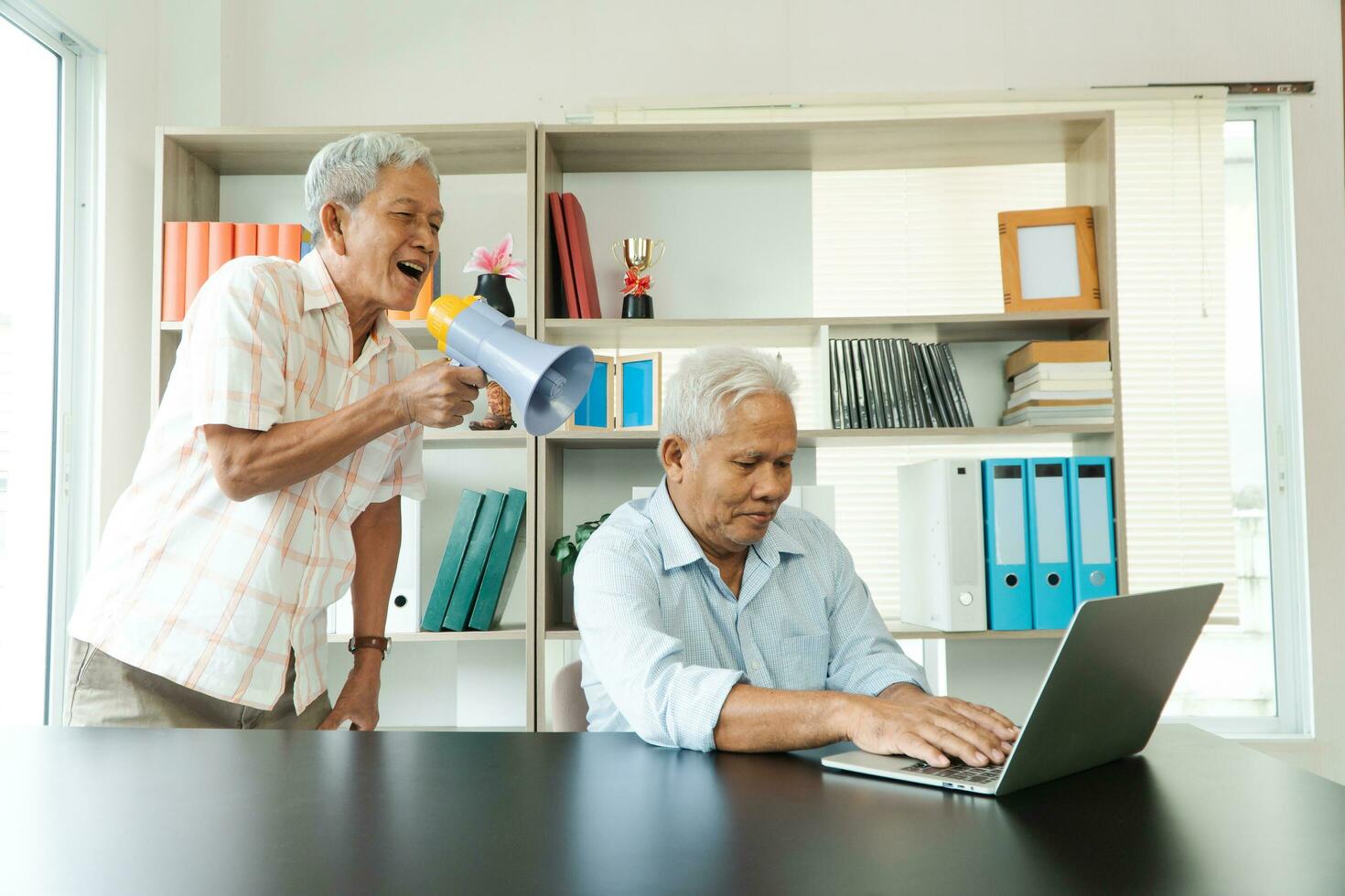 Old Asian elderly yell to a megaphone to talk with a friend for communication. Concept of communication problem in aging cause of ear be without hearing, deaf photo