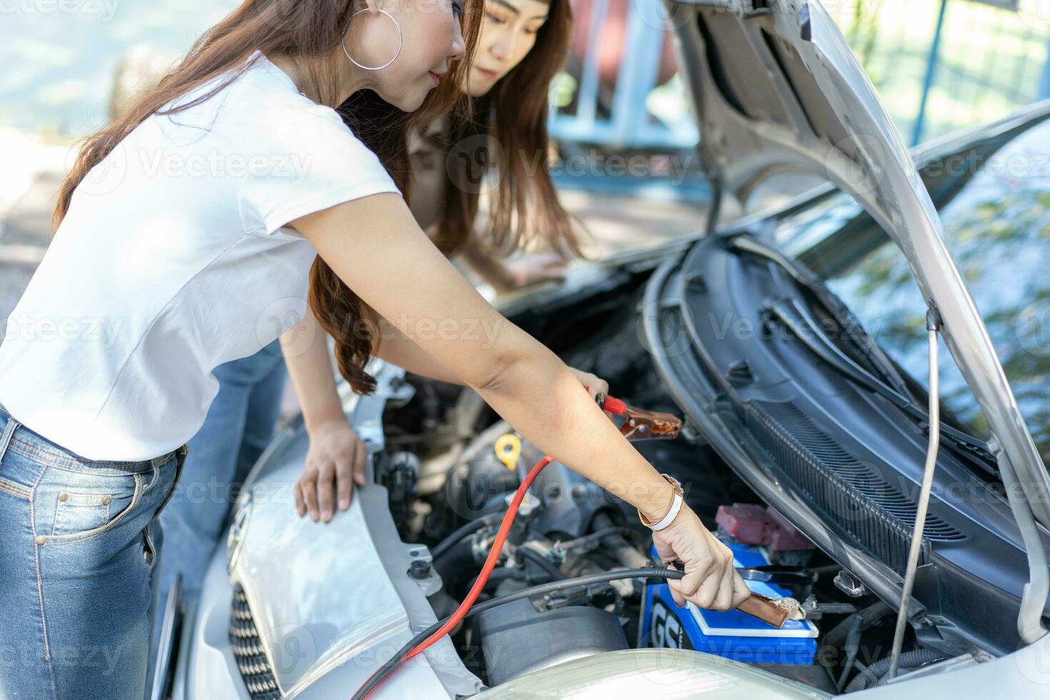 dos asiático personas tratar a cheque el coche motor y Espere para asistencia después un coche Descompostura en calle. concepto de un vehículo motor problema o accidente y emergencia ayuda desde un profesional mecánico foto