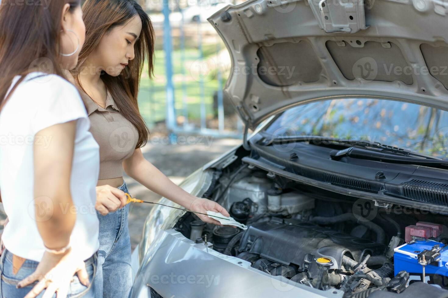 Two Asian people try to check the car engine and wait for assistance after a car breakdown on street. Concept of a vehicle engine problem or accident and emergency help from a Professional mechanic photo