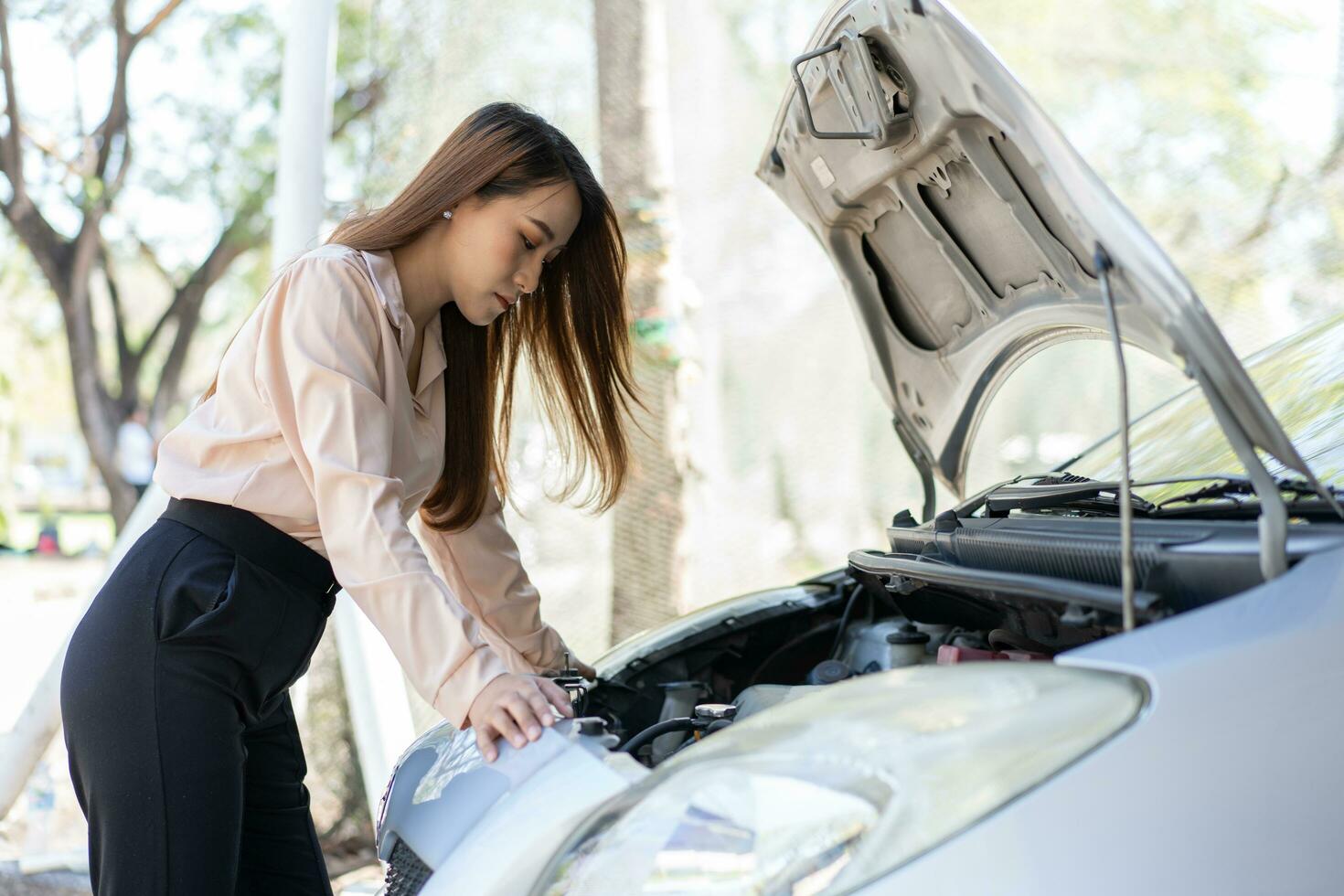 Angry Asian woman using a smartphone VIDEO conference for assistance after a car breakdown on street. Concept of a vehicle engine problem or accident and emergency help from a Professional mechanic photo