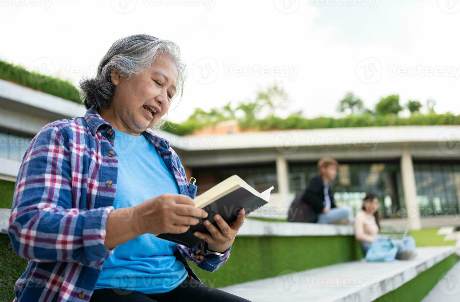 maduro adulto estudiante sentado en frente apagado Universidad edificio y leyendo colegio libros después asistiendo un Universidad clase, adulto educación aprendizaje estudiando contento asiático mayor retirado actividad foto