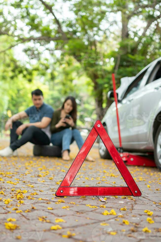 asiático Pareja utilizando teléfono inteligente para asistencia después un coche Descompostura en calle. concepto de vehículo motor problema o accidente y emergencia ayuda desde profesional mecánico foto