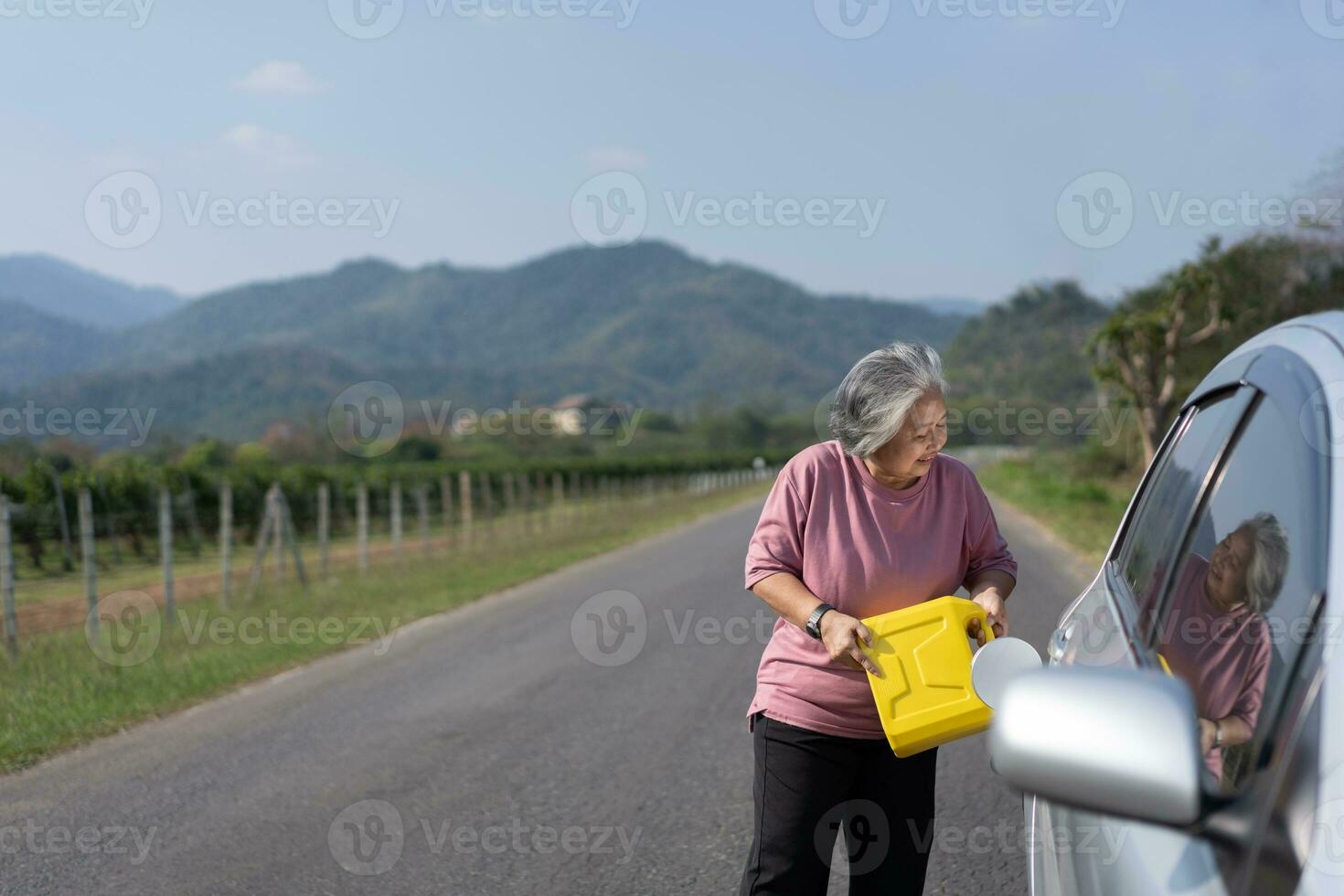 The car ran out of gas and stalled beside the road in suburbs and an elderly Asian woman used a gallon of spare gas to fuel the car. A woman prepares a gallon of spare gas to fuel before traveling. photo