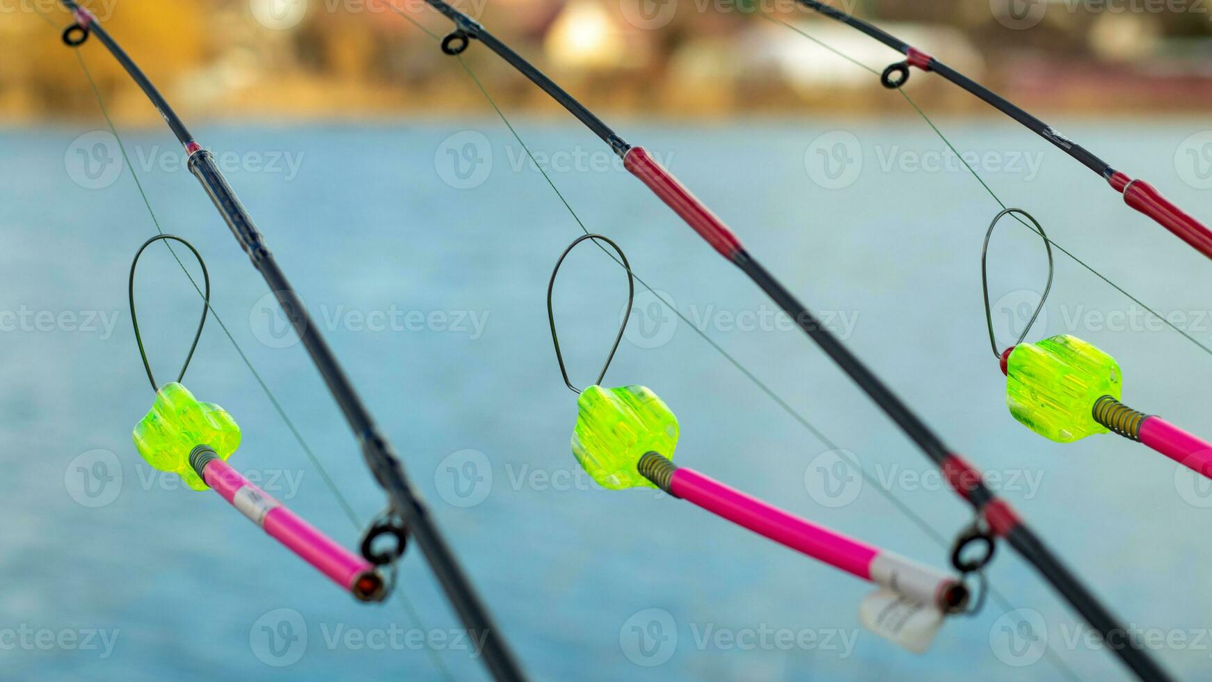 The bite alarm hangs on a fishing rod against the background of water.  Fishing rod while