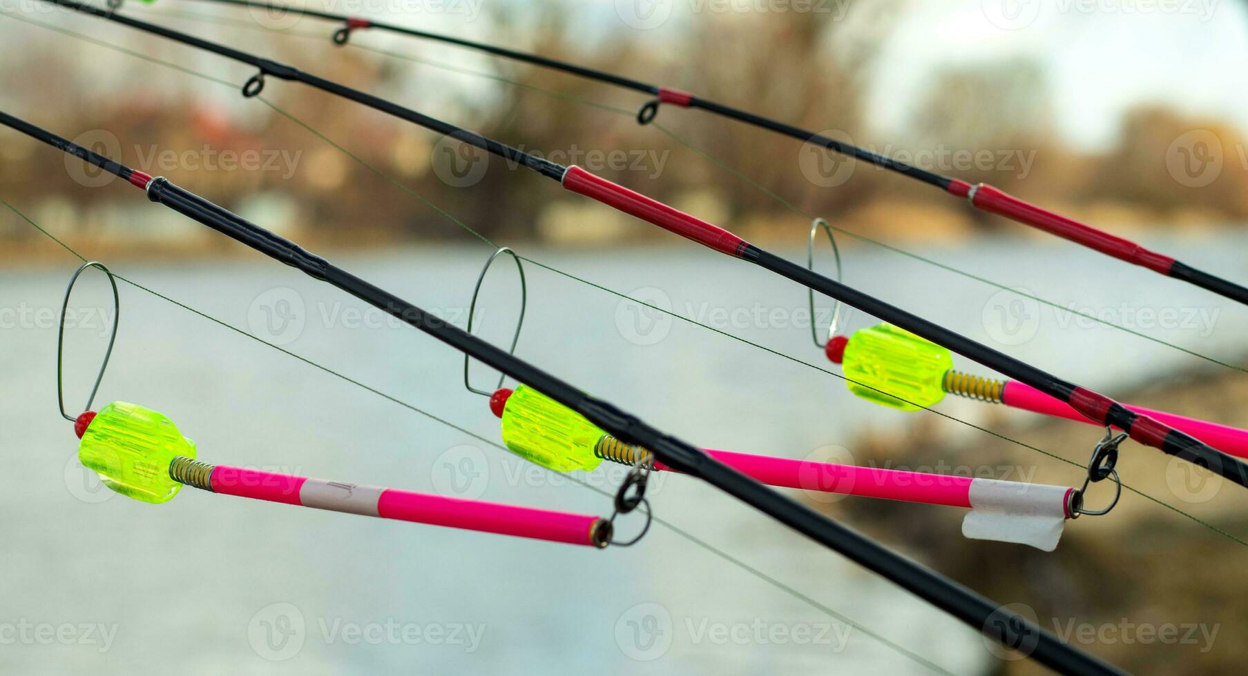 The bite alarm hangs on a fishing rod against the background of water. Fishing rod while fishing on the lake, river. Fishing tackle. Carp rod on a stand with a bite alarm on the line. photo