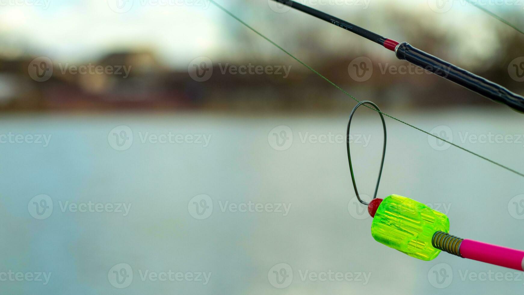 The bite alarm hangs on a fishing rod against the background of water. Fishing rod while fishing on the lake, river. Fishing tackle. Carp rod on a stand with a bite alarm on the line. photo