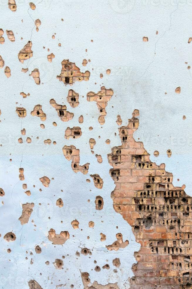 The wall of a building battered by rocket fragments in a war zone. Shelled wall. Facade of a bombed-out building. Armed conflict in Ukraine. Damage to the house as a result of artillery shelling. photo
