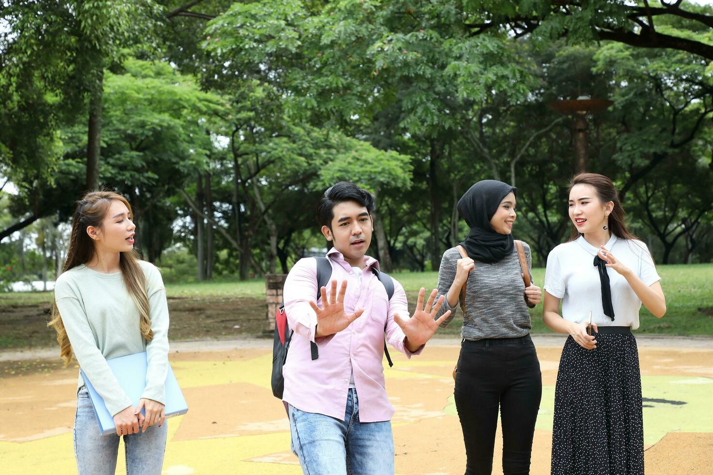 joven asiático malayo chino hombre mujer al aire libre parque caminar estar estudiar hablar discutir punto ordenador portátil archivo libro mochila foto