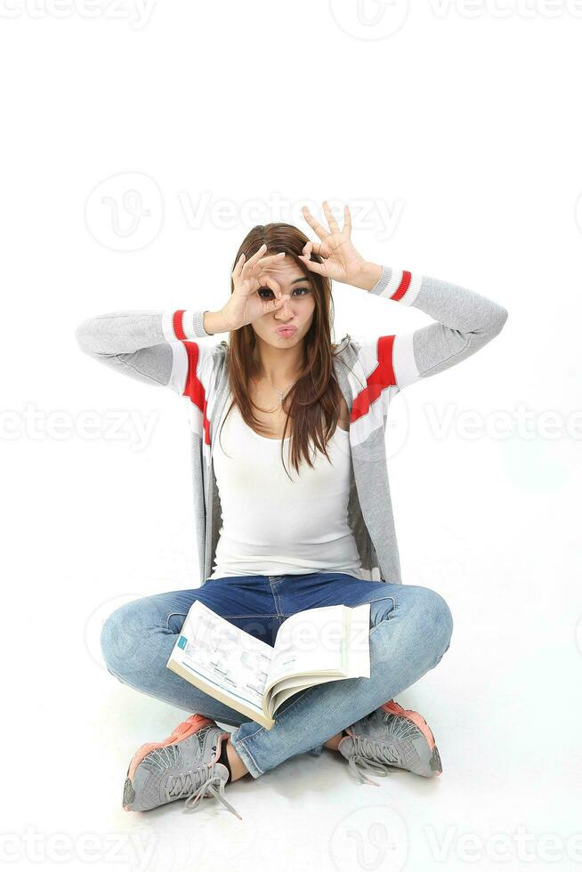 Yong Asian youth girl in casual dress sit on floor book on lap look through hole in hand ok sign expression funny witty on white background photo