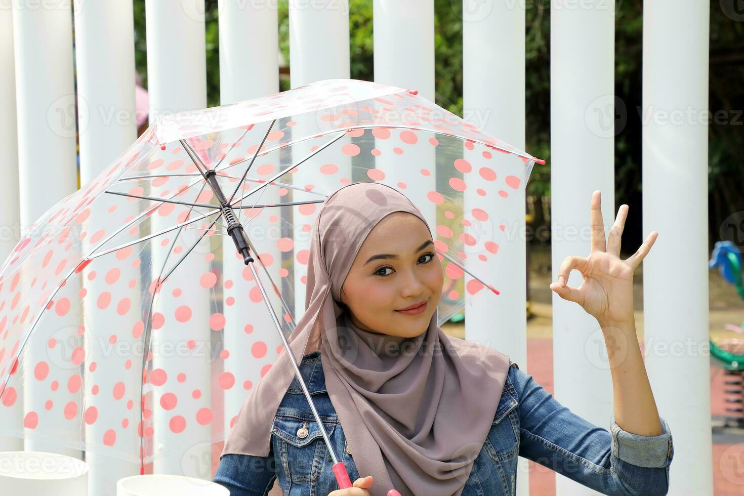 Young Asian Malay muslim woman headscarf outdoor green pose with umbrella ok finger sing photo