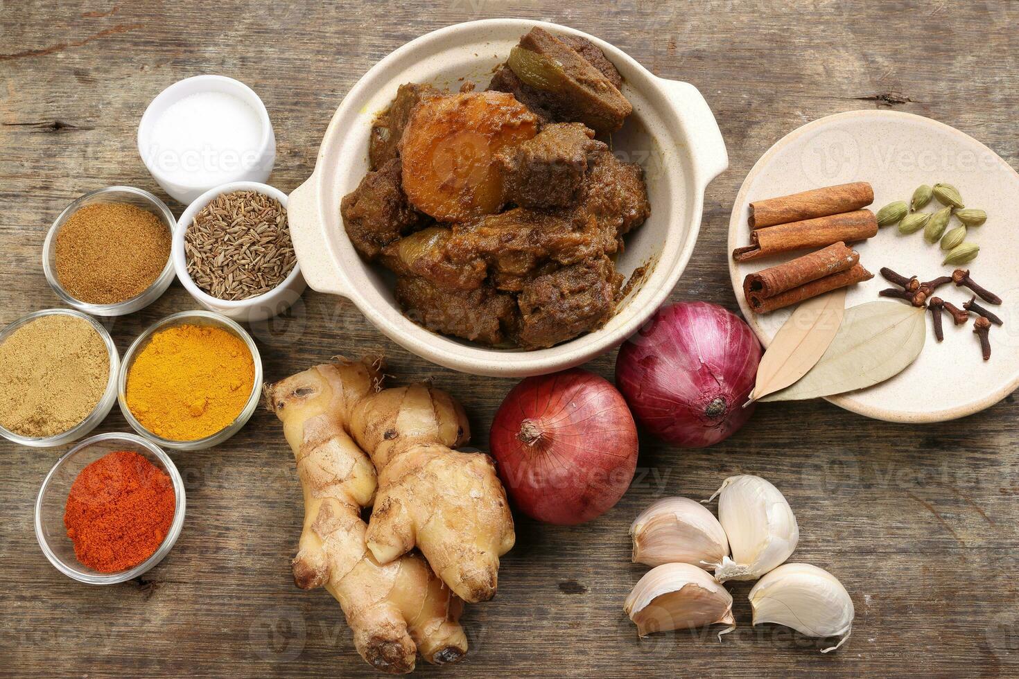 Beef bhuna dry curry with potato in ceramic bowl ingredients chilli cumin coriander turmeric powered salt onion garlic ginger bay leaf cinnamon cardamom clove over rustic wood background photo
