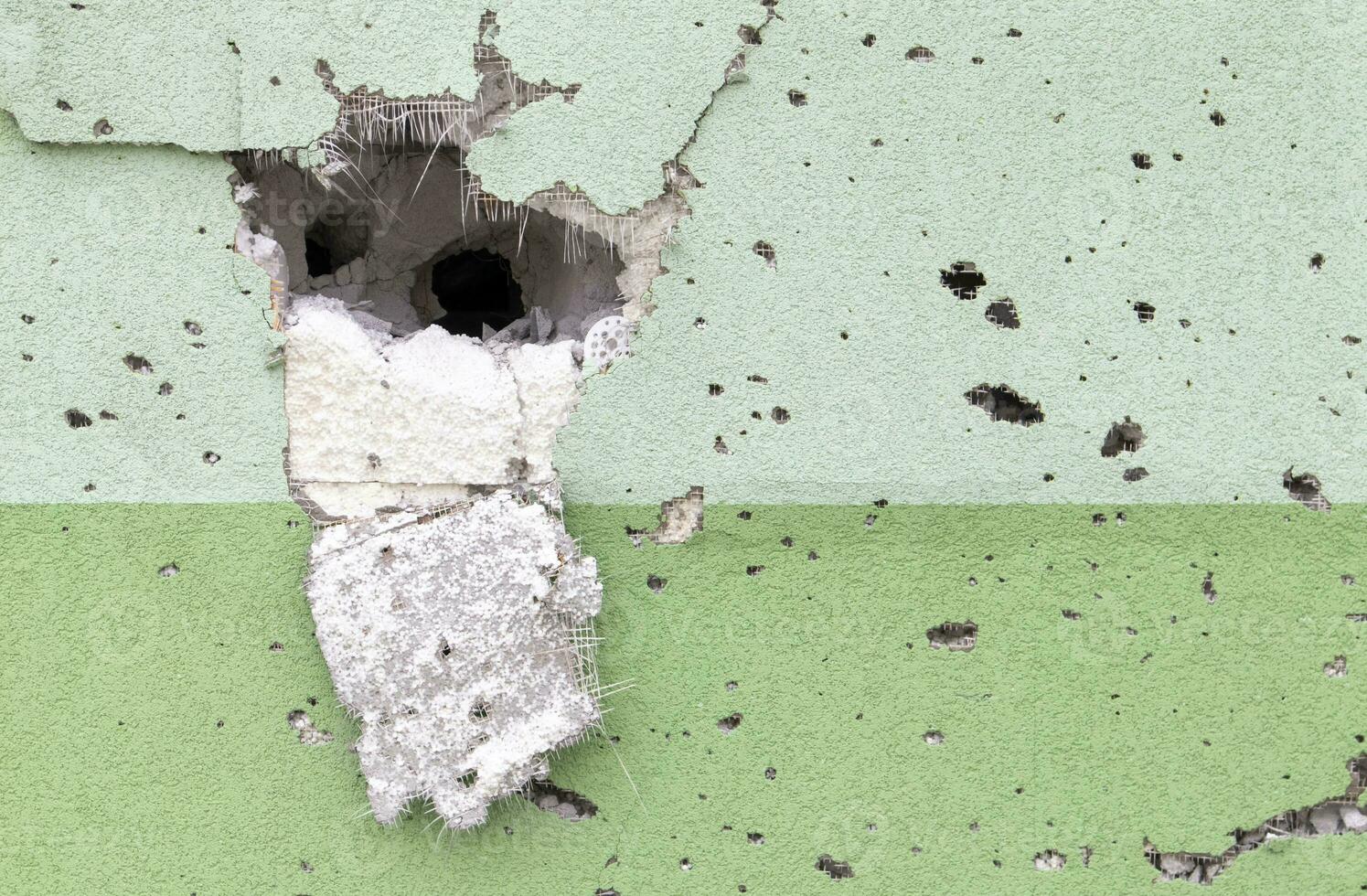 Holes from bullets and shrapnel in the wall on the front line. Scars of war. Concrete wall of a residential building with potholes and holes from gunfire. Consequences of the war in Ukraine. photo