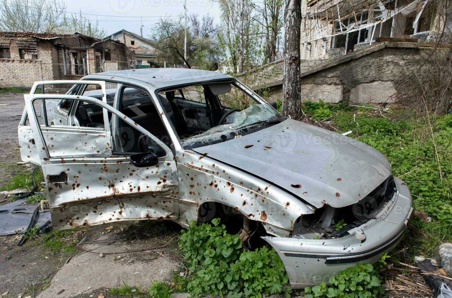 The car that burned down after the bombing of the city stands in the courtyard of a destroyed house. War between Russia and Ukraine. Fragments of a car after artillery shelling. photo