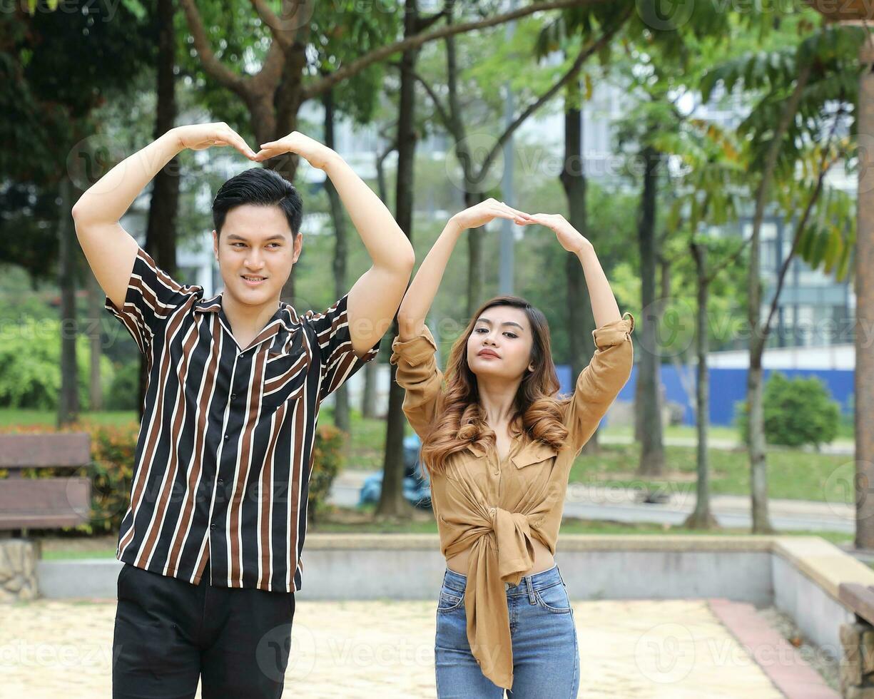 Young Asian Malay man woman outdoor green park walk talk discuss mingle happy joy hand on head hart shape dance photo