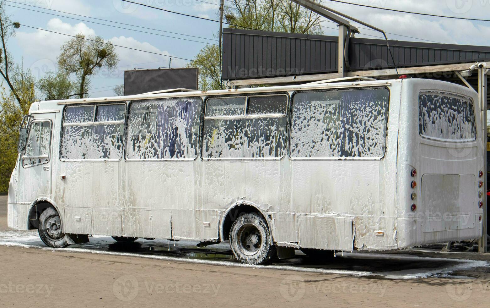 grande blanco autobús en espuma a un autoservicio coche lavar. externo Lavado de público transporte autobuses autoservicio manual alta presión coche lavar en el abierto aire. foto