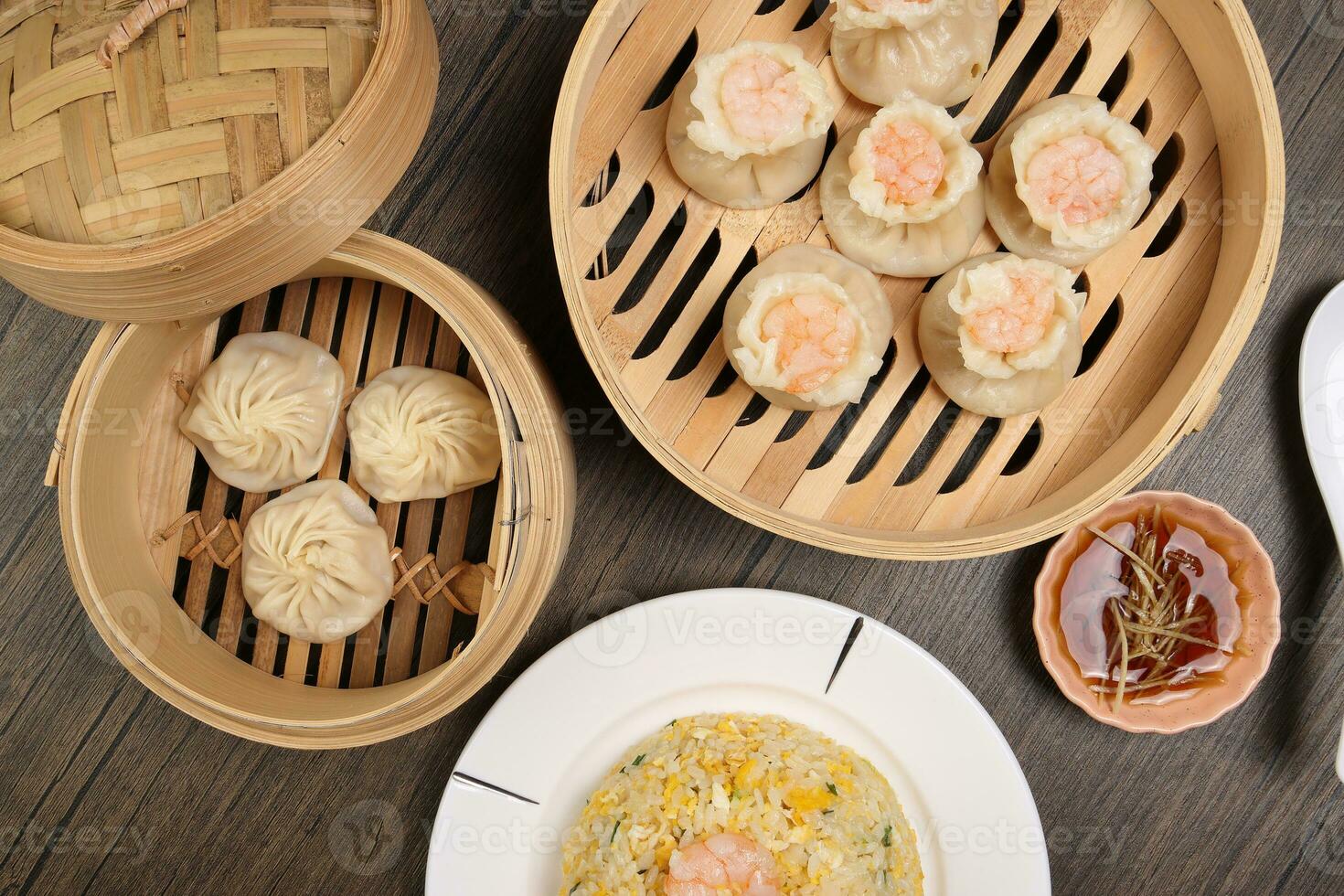 Prawn shrimp shaomai Xiao long bao dim sum dumpling chicken prawn fish seafood vegetable in bamboo steamer fried rice on plate sauce chopsticks soup spoon over rustic background photo