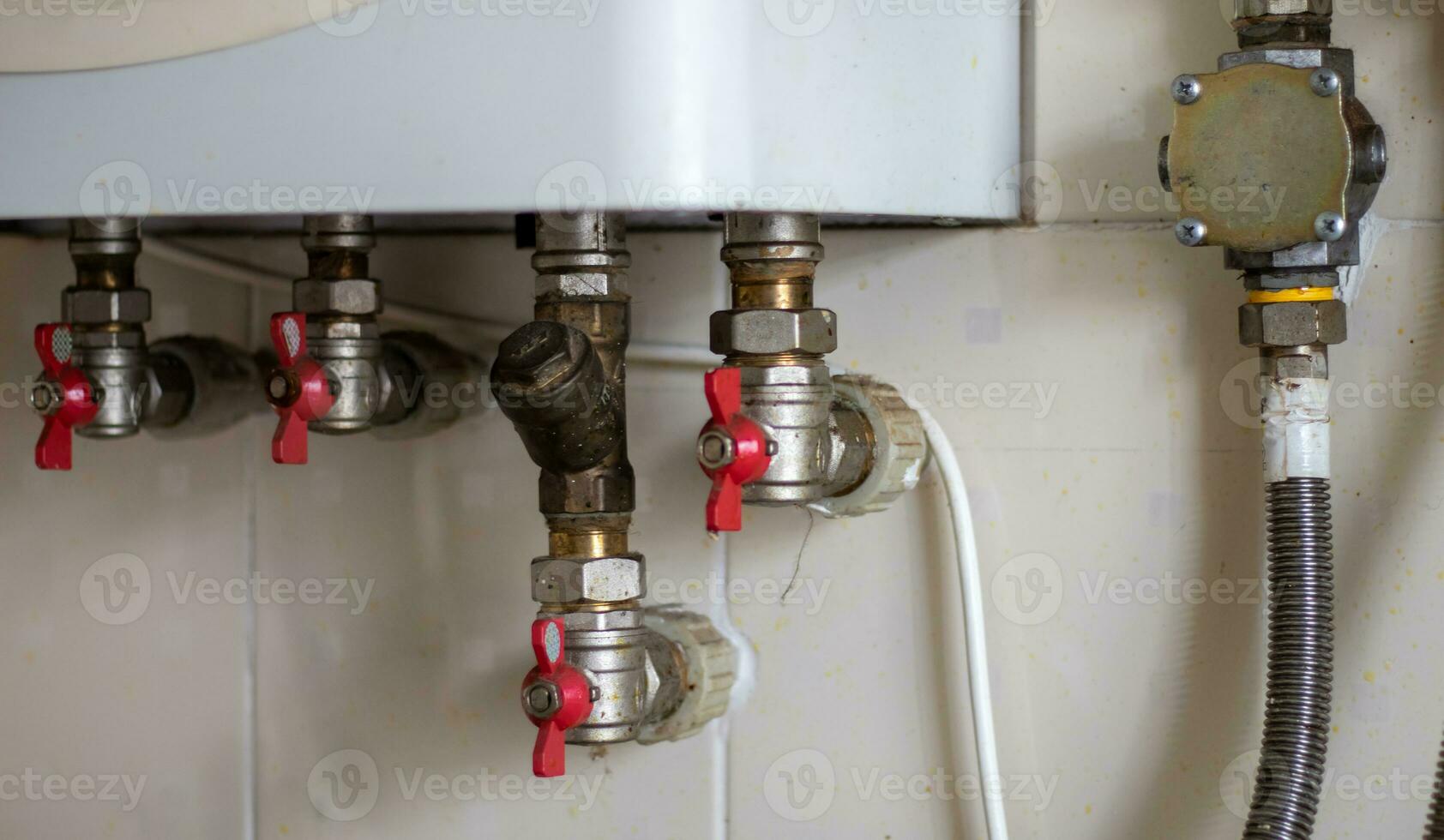 Hidden water taps for connecting a gas boiler on a tiled wall. Plumbing connections for a domestic double-circuit gas boiler. Pipes of the heating system. Installing a gas boiler with red taps. photo