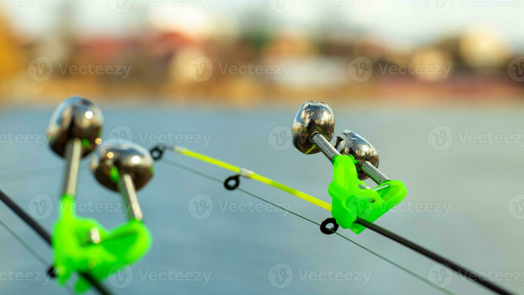 The bite alarm hangs on the tip of the fishing rod against the background of water. Fishing rod while fishing on the lake, river. Fishing tackle. Two rods with bite alarm. photo