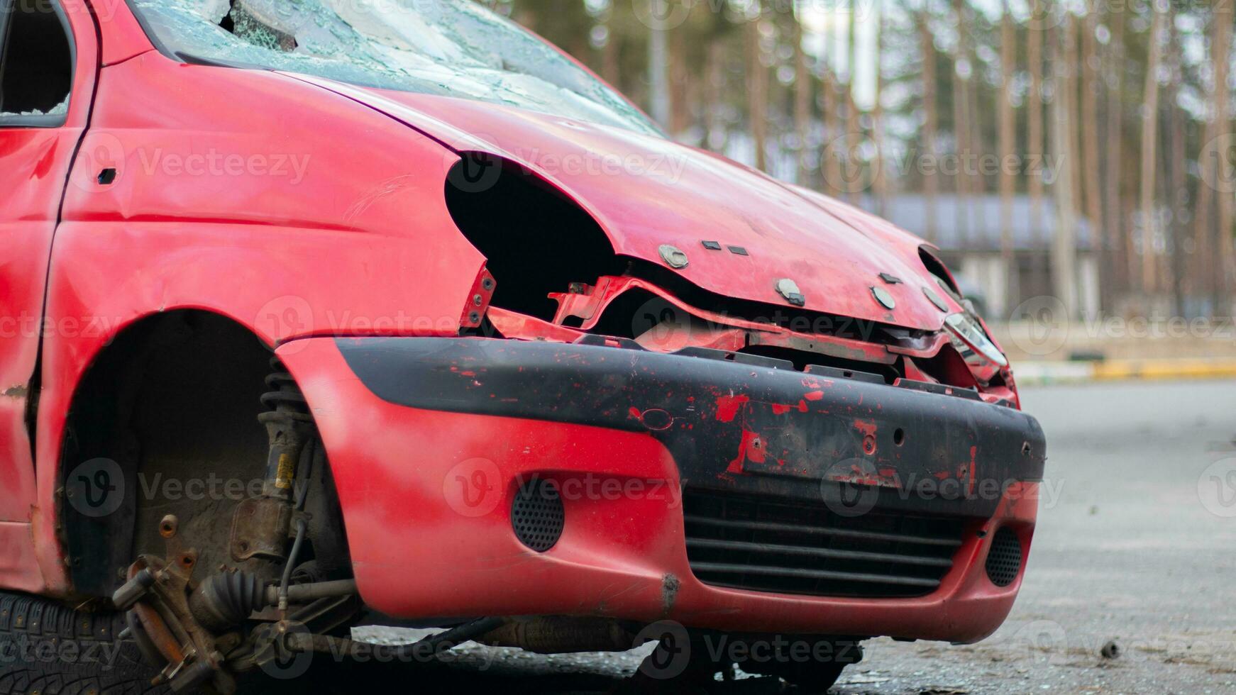 un roto, arrugado pequeño rojo coche soportes en el lado de el la carretera sin faros y un rueda después un poderoso explotar. accidente en el calle, dañado coche después un colisión en el ciudad. foto