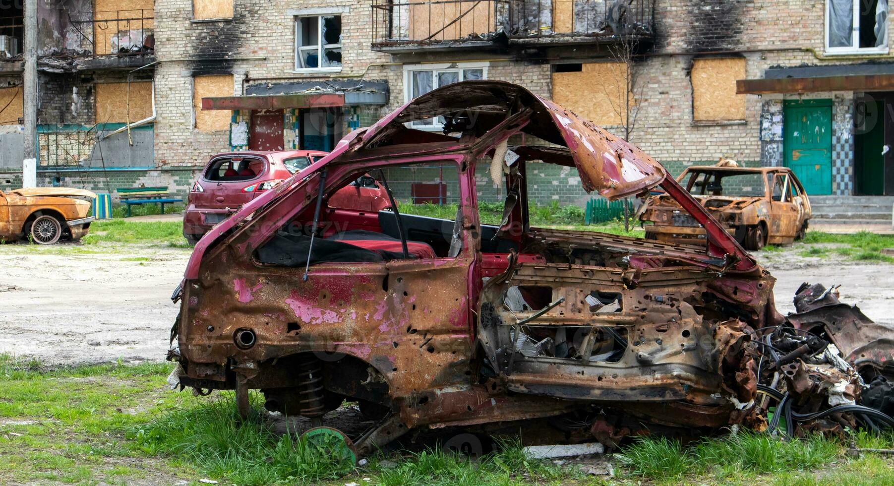 The car that burned down after the bombing of the city stands in the courtyard of a destroyed house. War between Russia and Ukraine. Fragments of a car after artillery shelling. photo