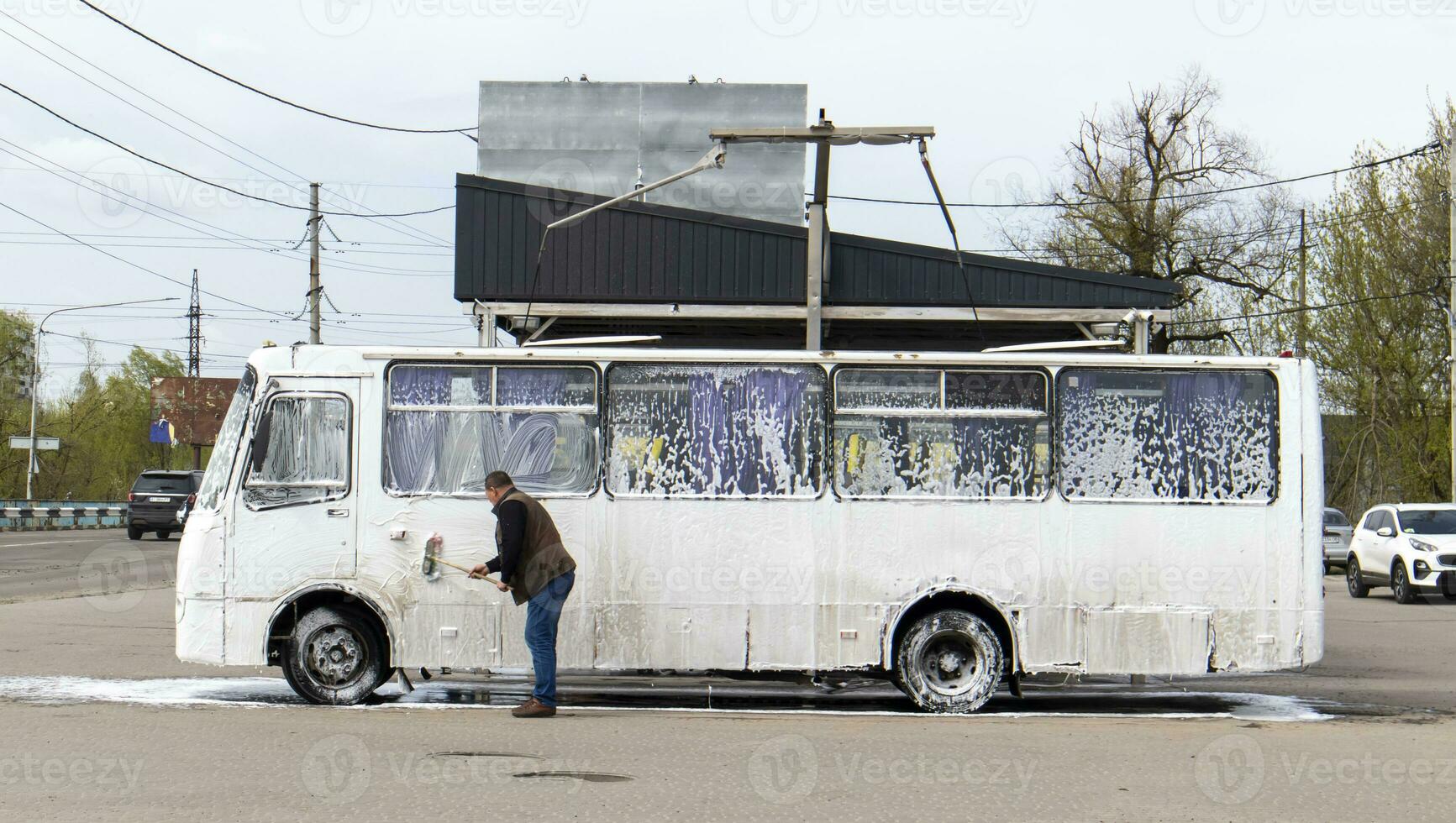 Big white bus in foam at a self-service car wash. External washing of public transport buses. Self-service manual high-pressure car wash in the open air. photo