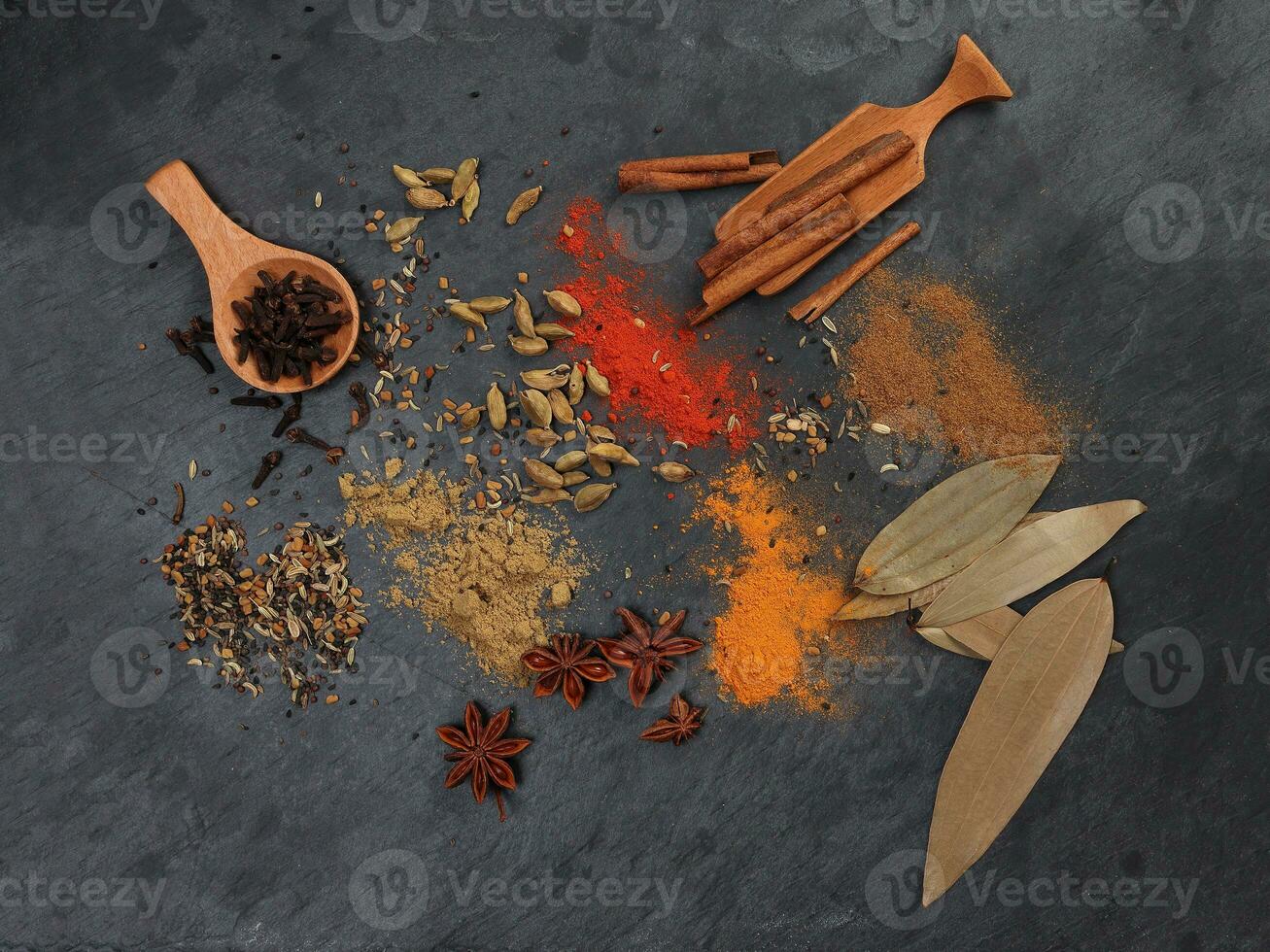 Mix variety spice cinnamon cardamom clove bay leaf wooden chilli cumin turmeric powered on black slate background photo