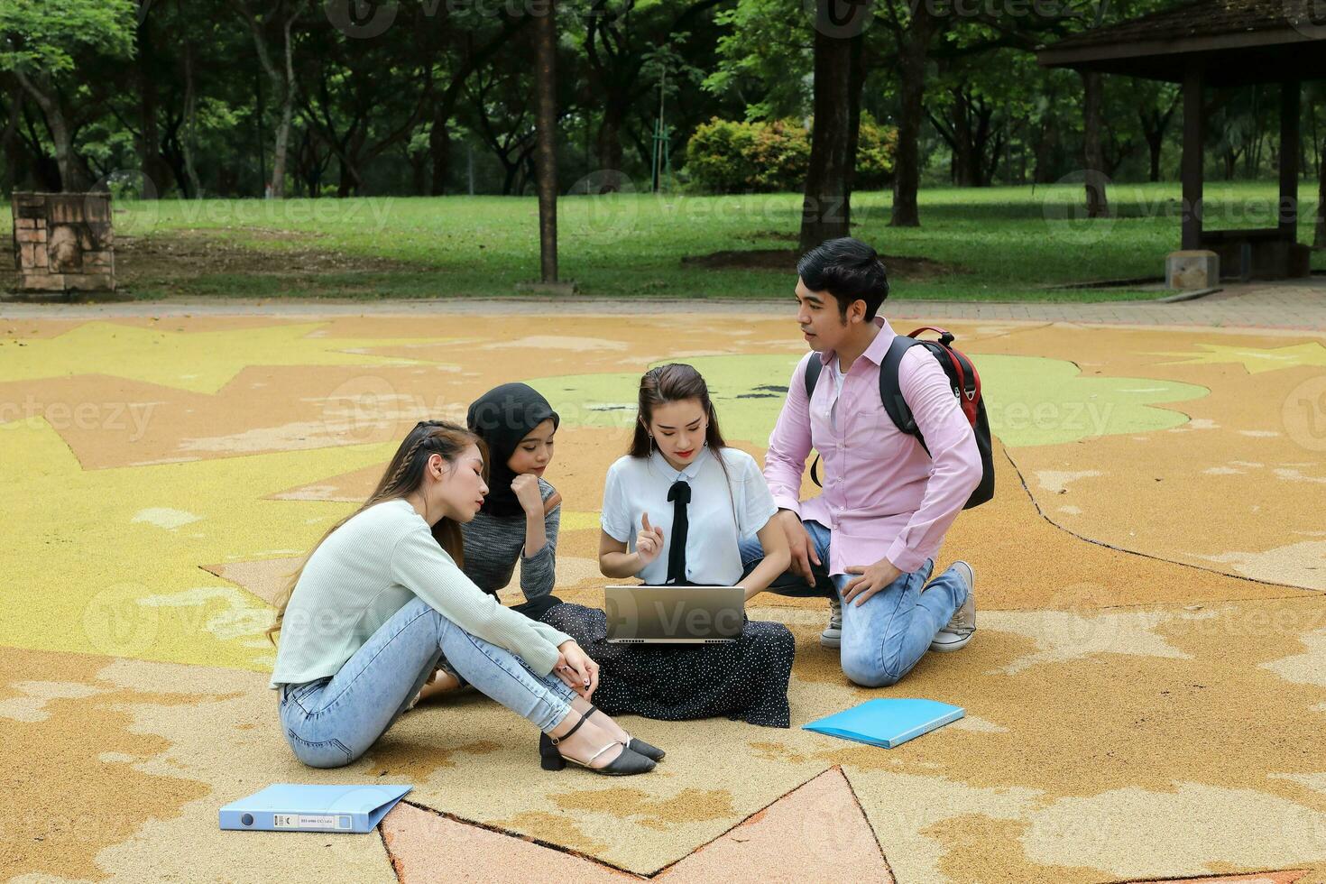Young asian malay chinese man woman outdoor park sit on ground study talk discuss point laptop file book backpack mingle fun meet photo