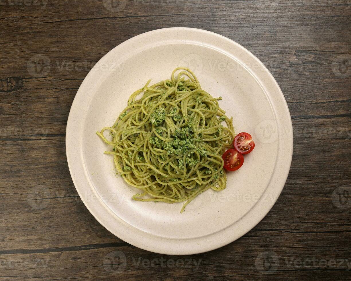 Asian style spaghetti with minced chicken spinach thai basil tomato garlic nutmeg olive oil presto sauce served on badge ceramic plate over on rustic wood background photo