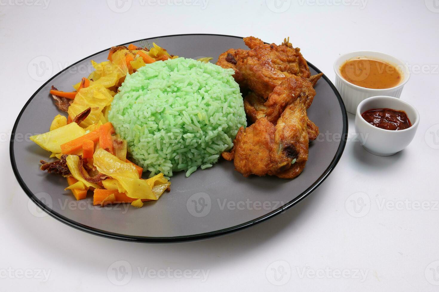 Steamed green rice spiced deep fried chicken cabbage carrot vegetable warung nasi ayam goreng on dark grey plate white background gravy sambal sauce photo