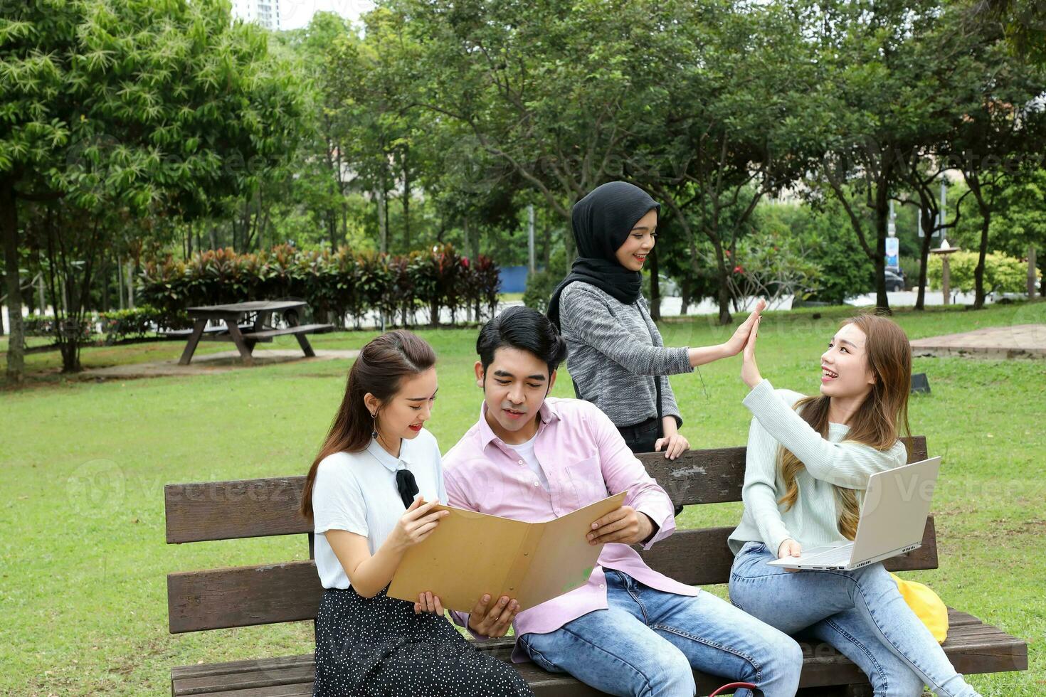 Young asian malay chinese man woman outdoor on park bench study talk discuss point laptop file book photo