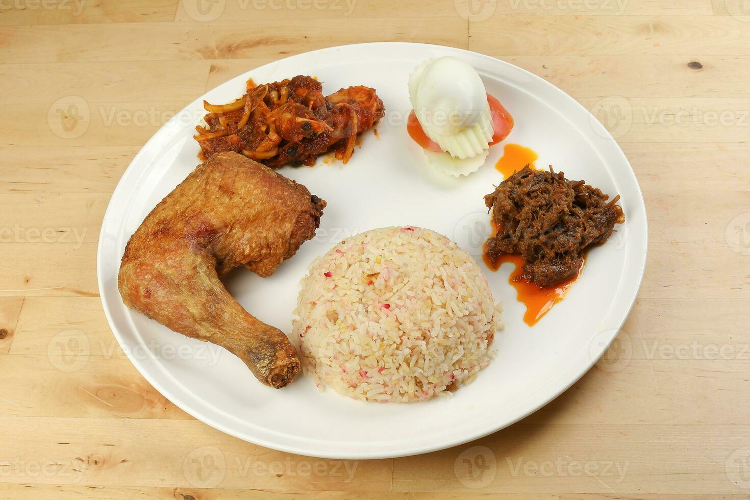 Indonesian royal dish nasi bojari with deep spiced deep fried chicken leg sambal prawn curry beef rendang boild egg cucumber and tomato slice photo