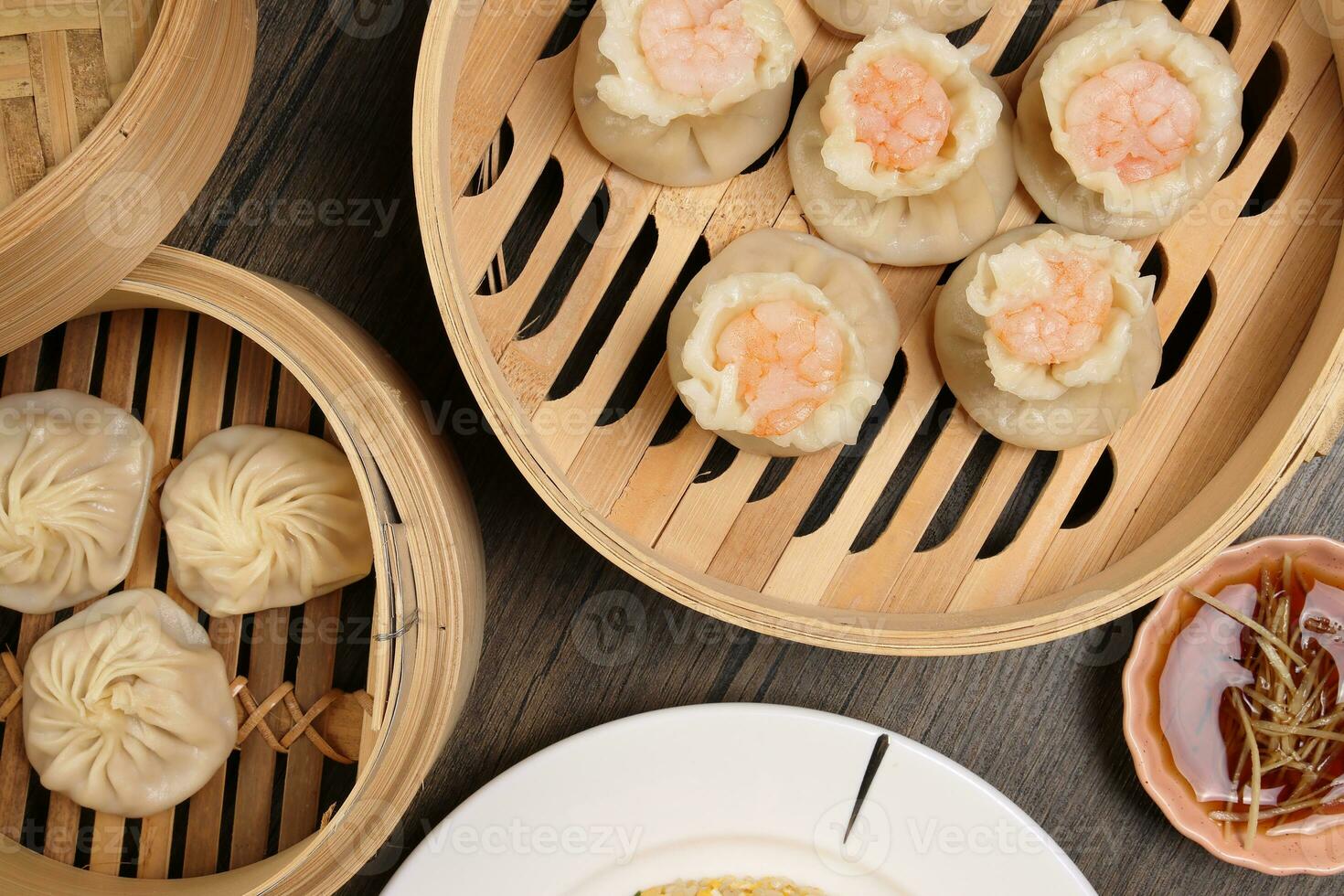 Prawn shrimp shaomai Xiao long bao dim sum dumpling chicken prawn fish seafood vegetable in bamboo steamer fried rice on plate sauce chopsticks soup spoon over rustic background photo