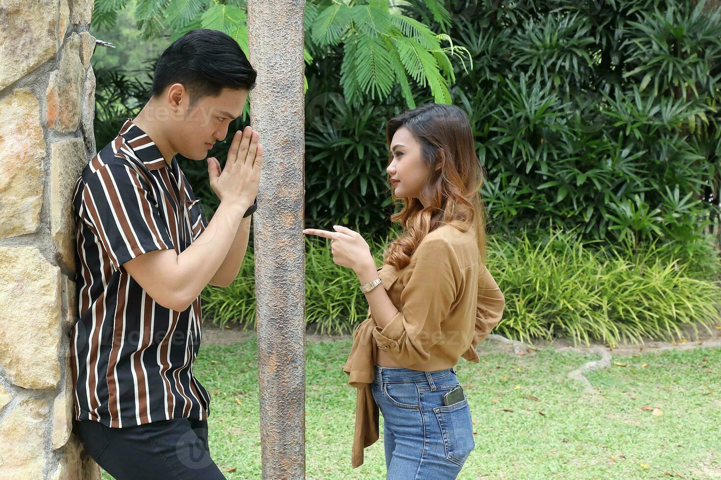 Young Asian Malay man woman outdoor green park walk talk discuss mingle under umbrella photo
