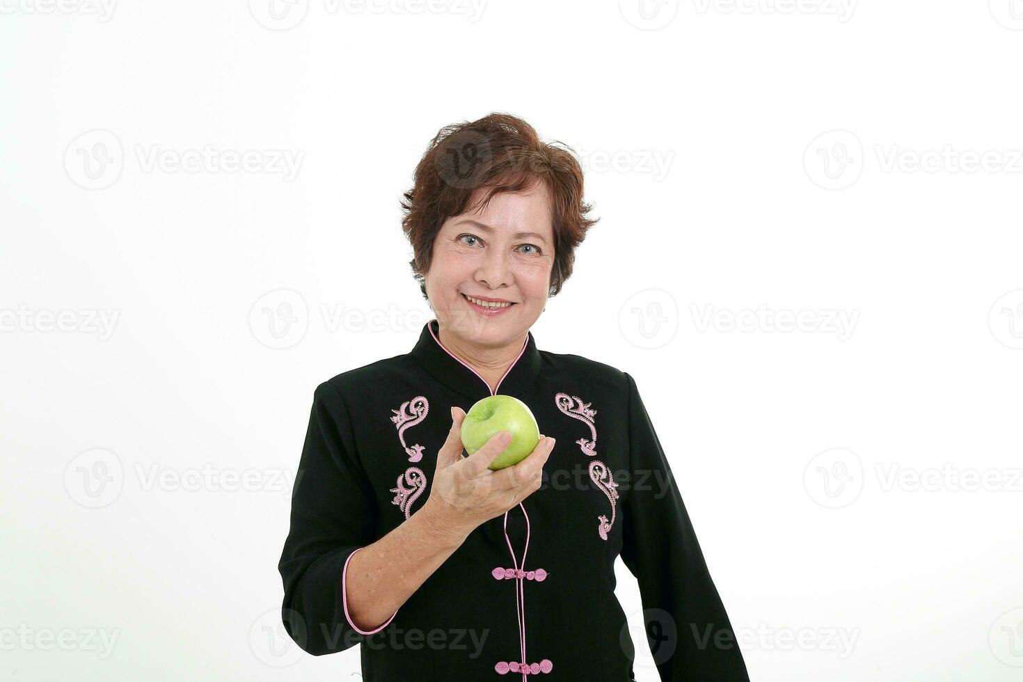 Elderly asian Chinese female wearing black tang samfu on white background holding green apple photo