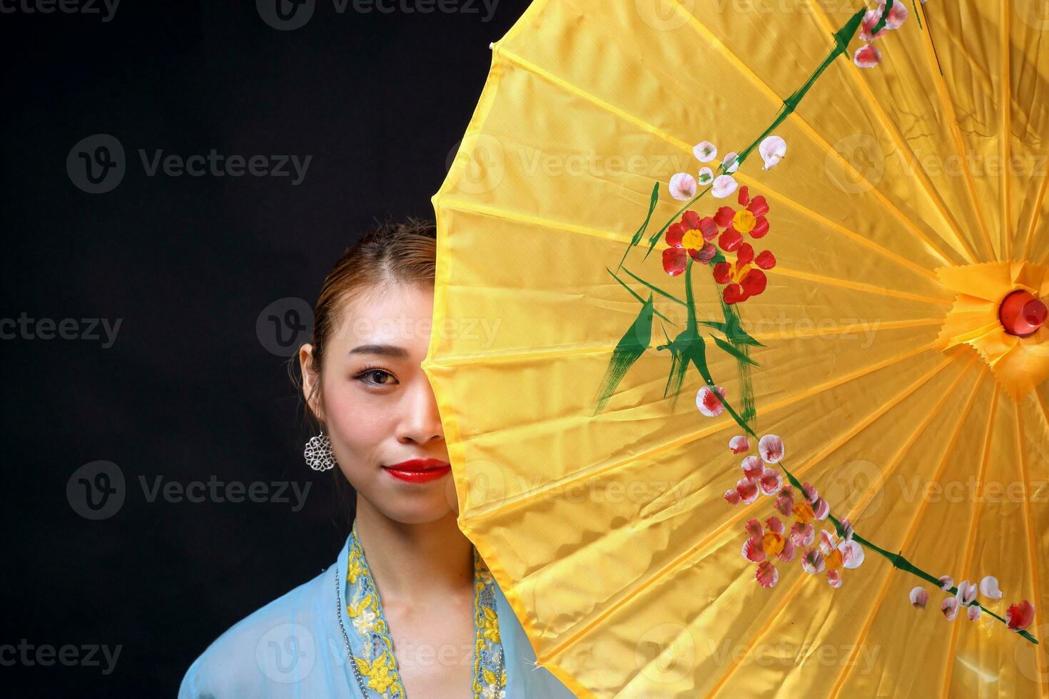 Asian woman in tractional kebaya behind umbrella on black background photo